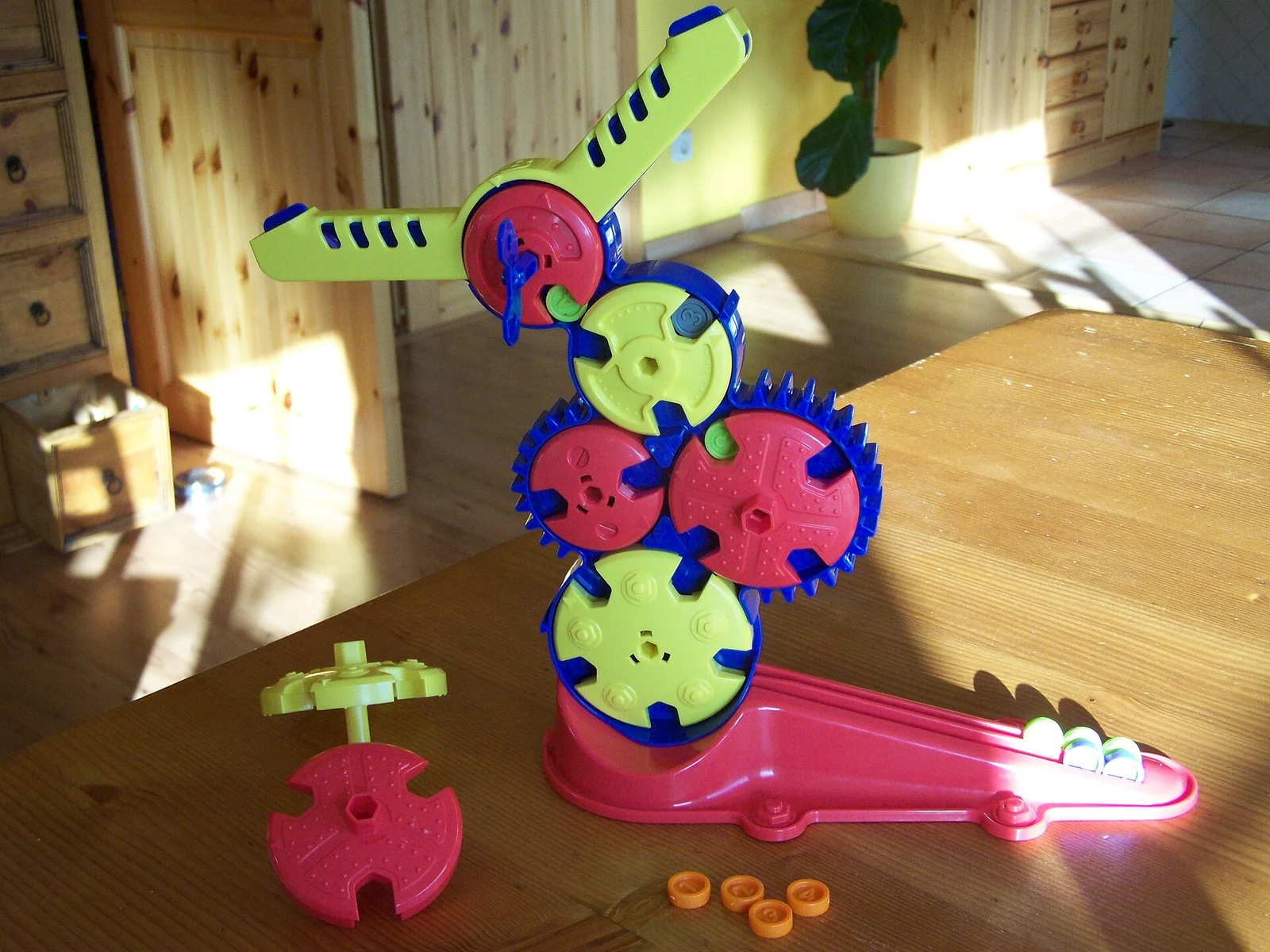 Farbiges Zahnrad-Geschicklichkeitsspiel auf einem Holztisch in einem Wohnraum mit gelben Spielchips.