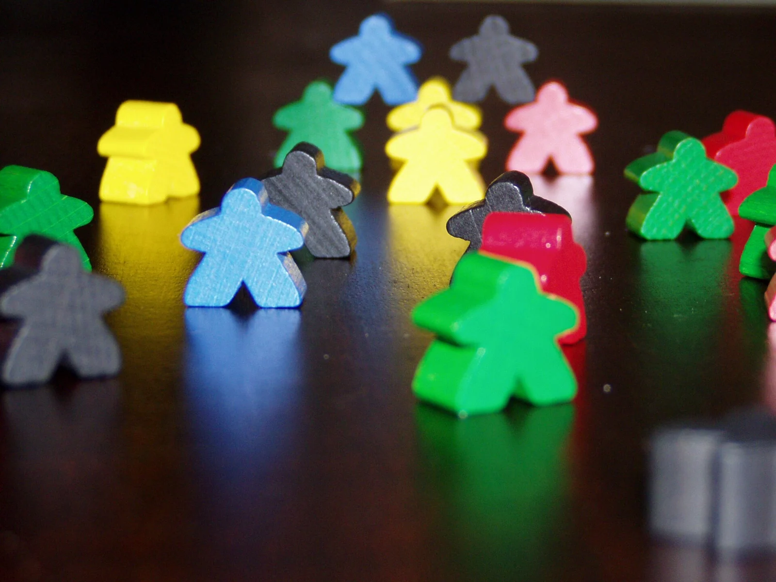 Bunte Meeple-Holzfiguren stehen auf einer dunklen Tischplatte.