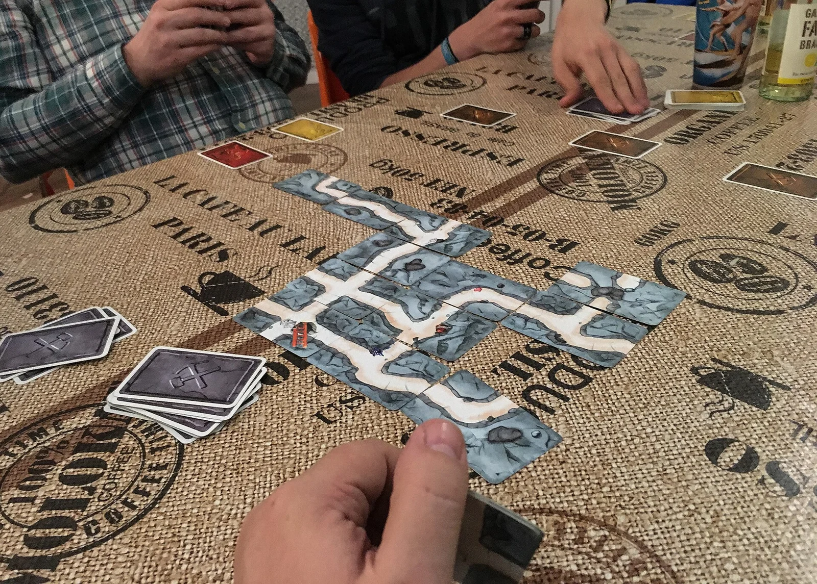 Auf einem Tisch ausgelegte Gang-Karten des Spiels Saboteur, Spieler halten Handkarten.