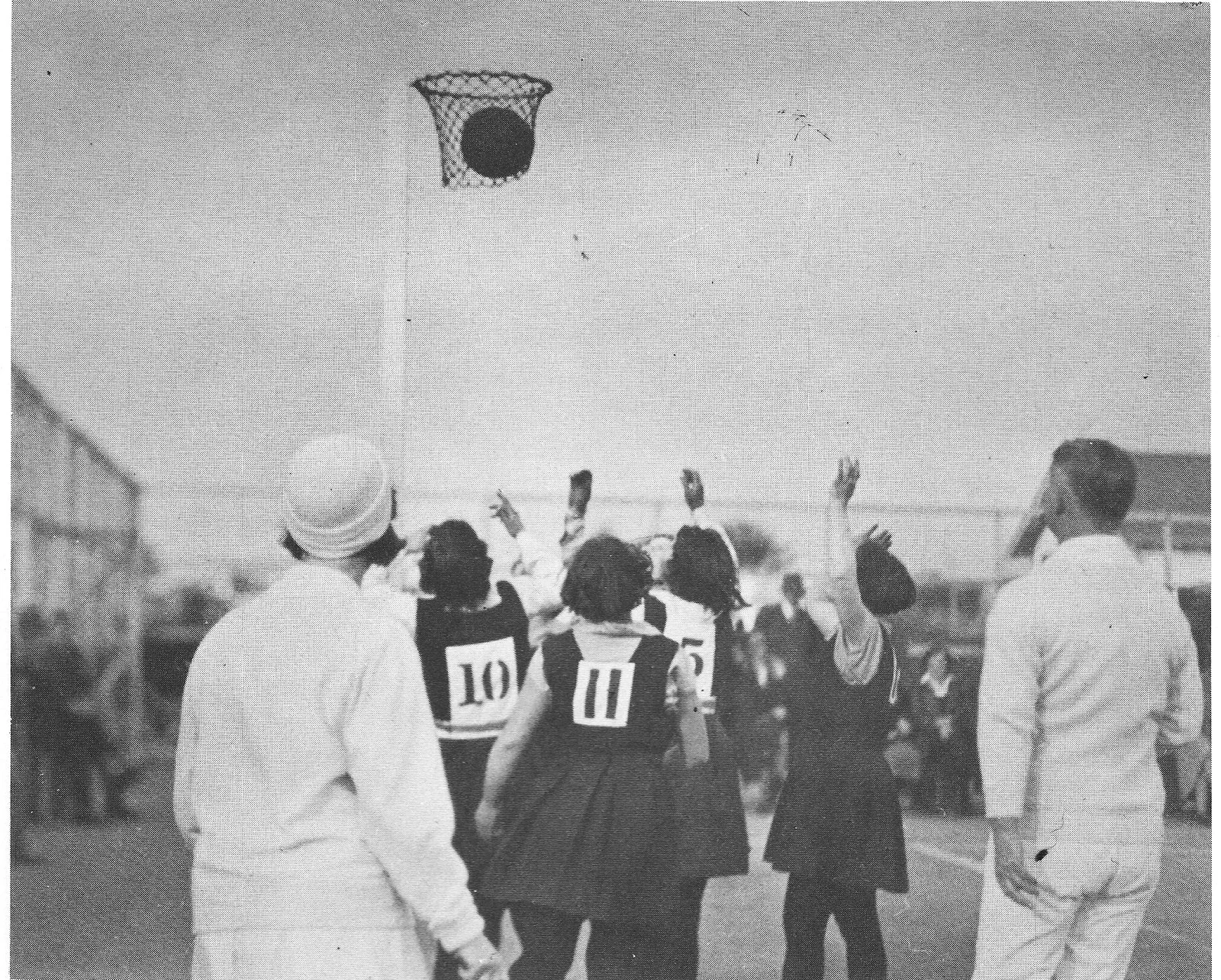 Historische Schwarz-Weiß-Aufnahme eines Netballspiels der 1920er Jahre mit Ball im Korb, Spielerinnen von hinten.