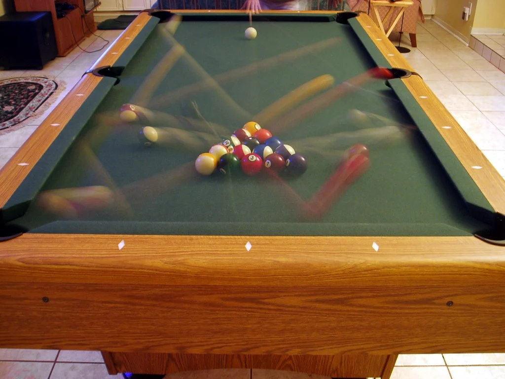 Poolbillardtisch mit angestoßenem Kugeldreieck und weißer Spielkugel in Langzeitbelichtung.