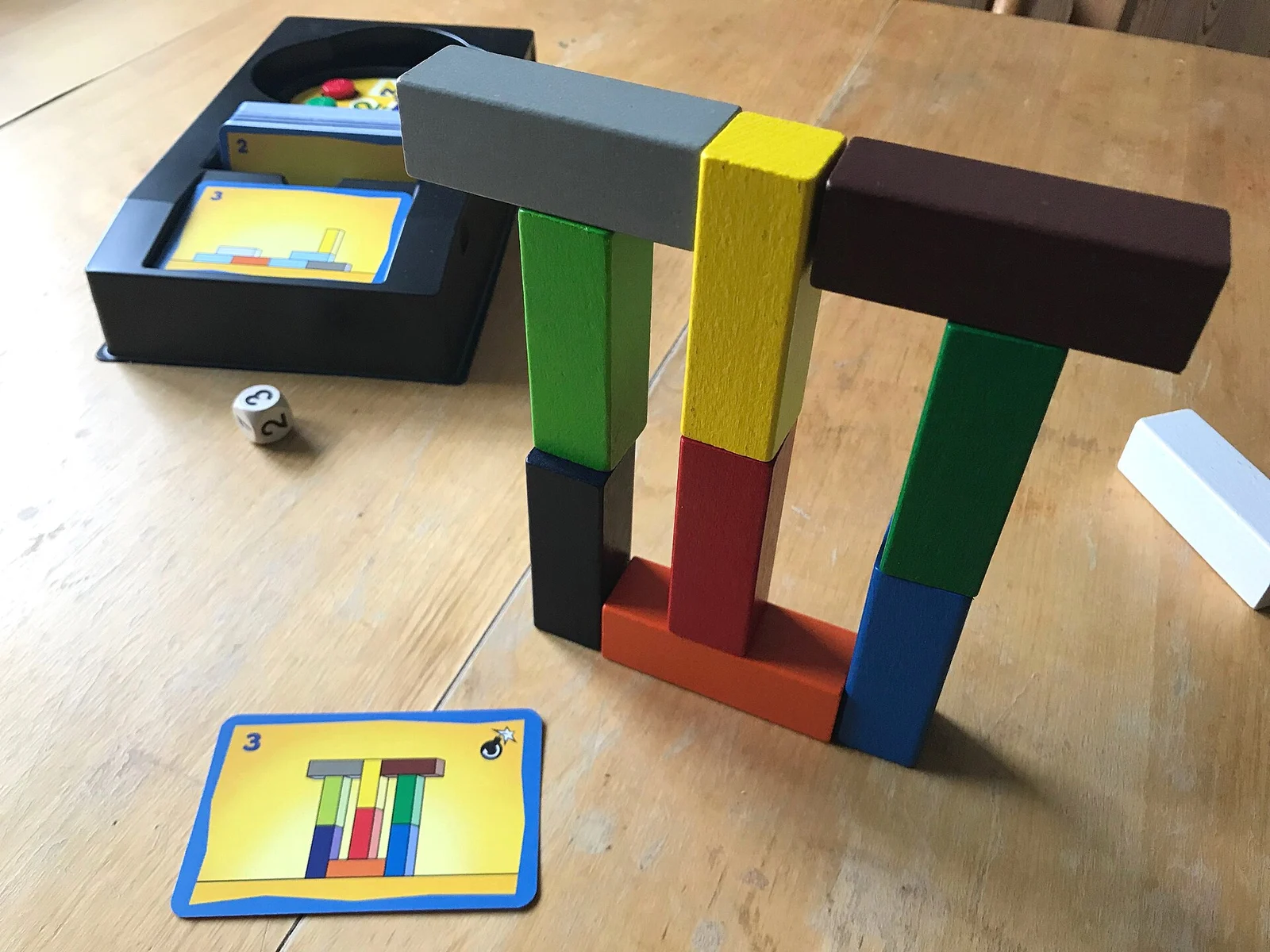 Bauwerk aus bunten Holzsteinen mit passender Vorlagekarte und Materialbox auf einem Holztisch.