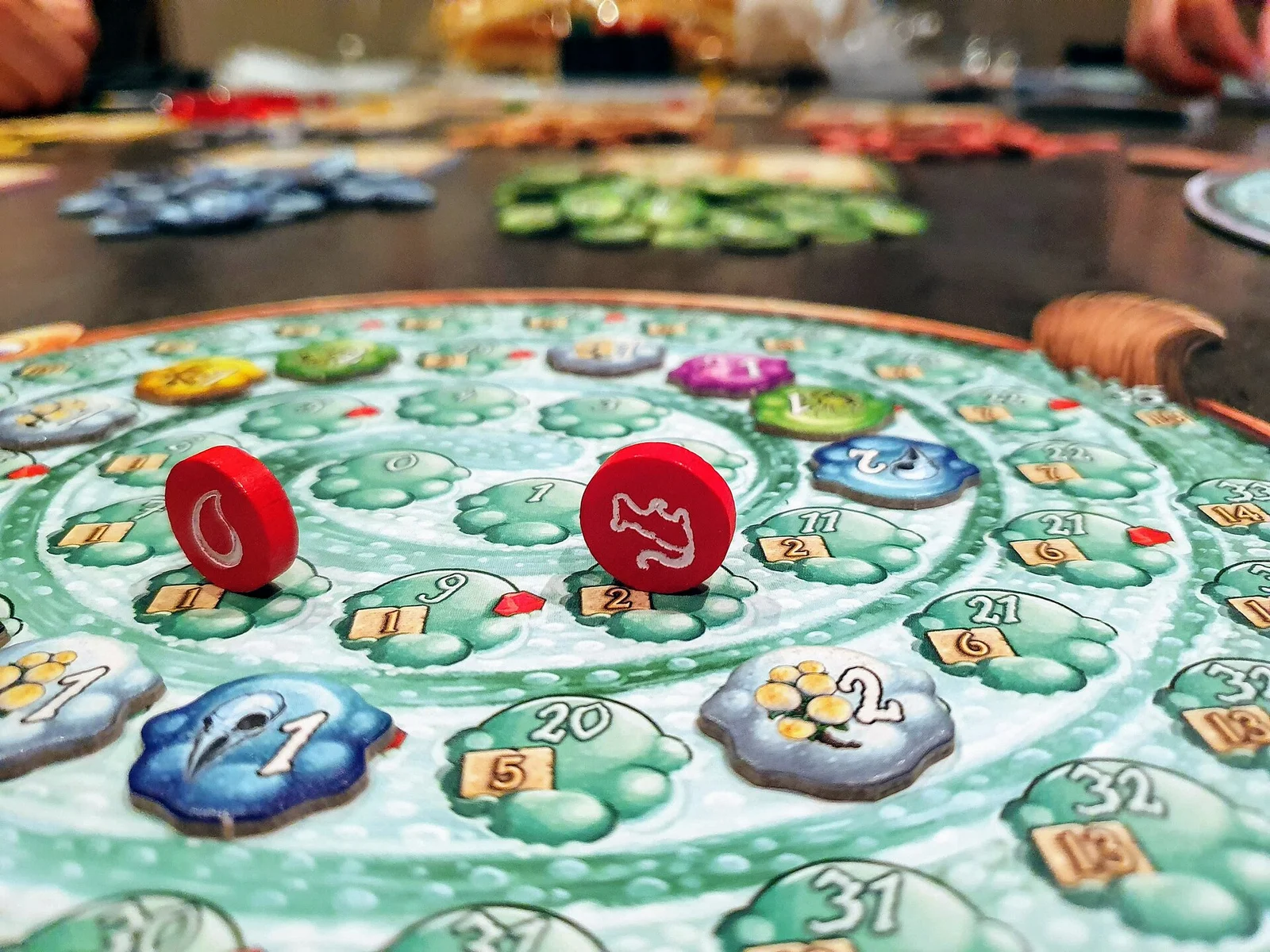 Nahaufnahme eines Quacksalber-Kessels mit roten Spielsteinen auf der Spirale, im Hintergrund weiteres Spielmaterial.