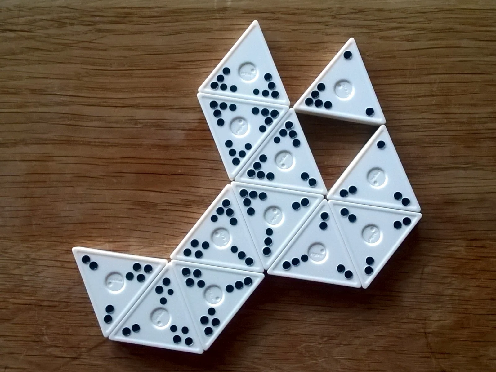 Weiße dreieckige Legesteine mit schwarzen Punkten statt Zahlen bilden eine Auslage auf einem Holztisch.
