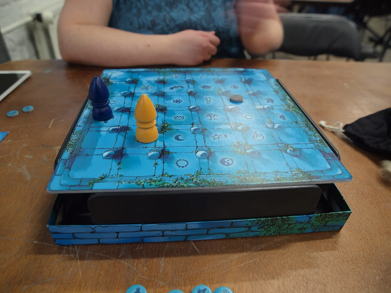 Spielbrett des Magischen Labyrinths mit blauer und gelber Spielfigur und Metallkugel auf einem Tisch.