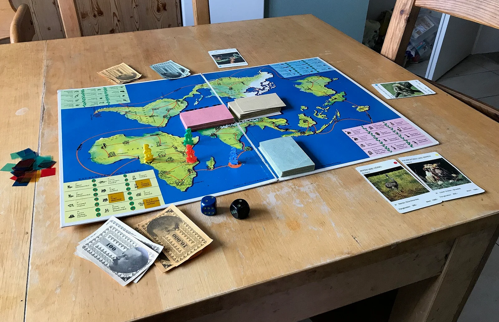 Aufgebautes Spiel mit Weltkartenplan, Karten, Spielgeld, Würfeln und Figuren auf einem Tisch.