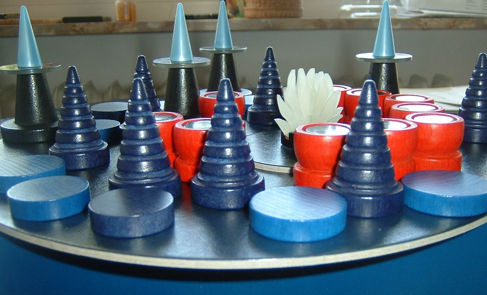 Nahaufnahme des Spielmaterials von Nacht der Magier: blaue Magierkegel, rote Kessel und blaue Holzplättchen auf einer erhöhten runden Spielfläche mit weißem Lichtring in der Mitte.