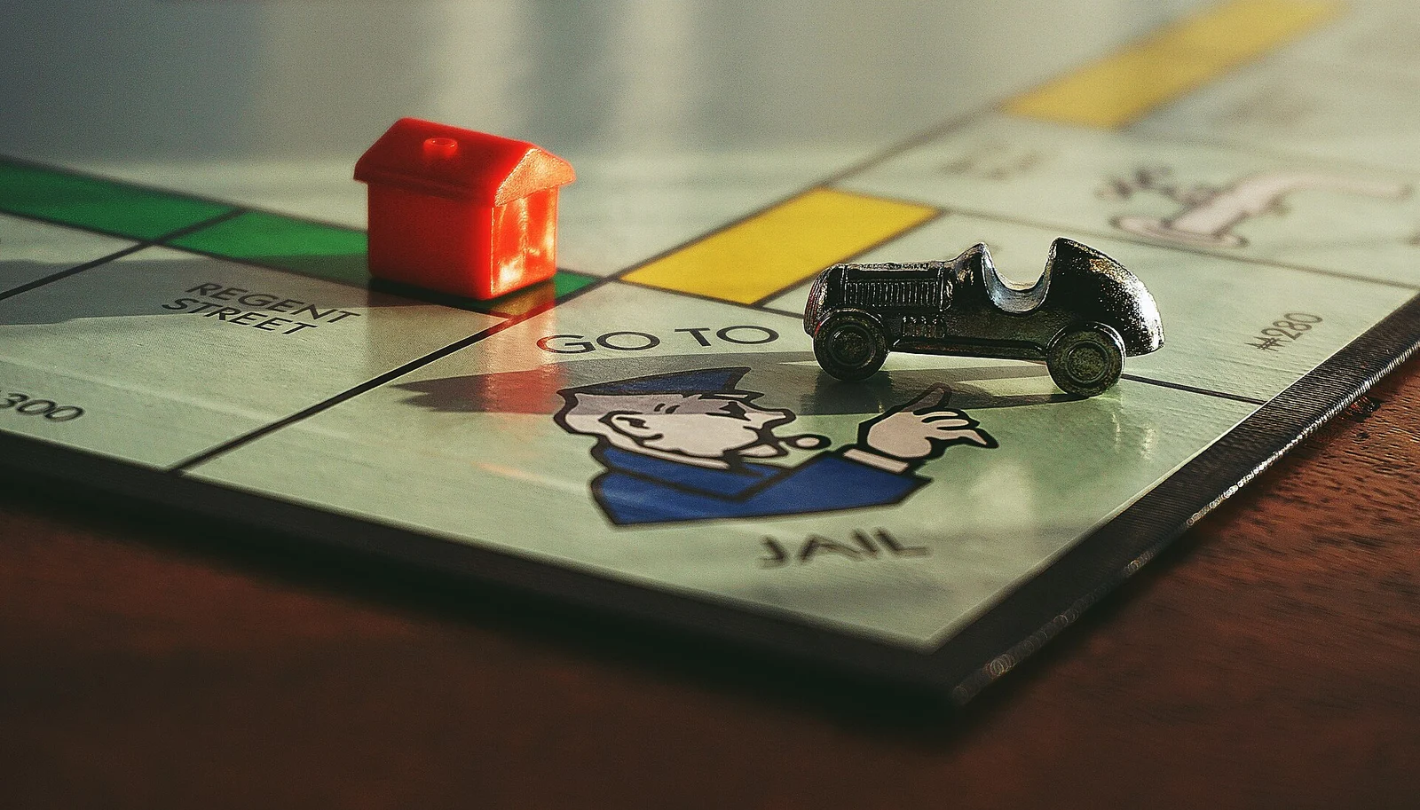 Nahaufnahme eines Monopoly-Spielbretts mit rotem Haus und Auto-Spielfigur nahe dem Feld 'Go to Jail'.
