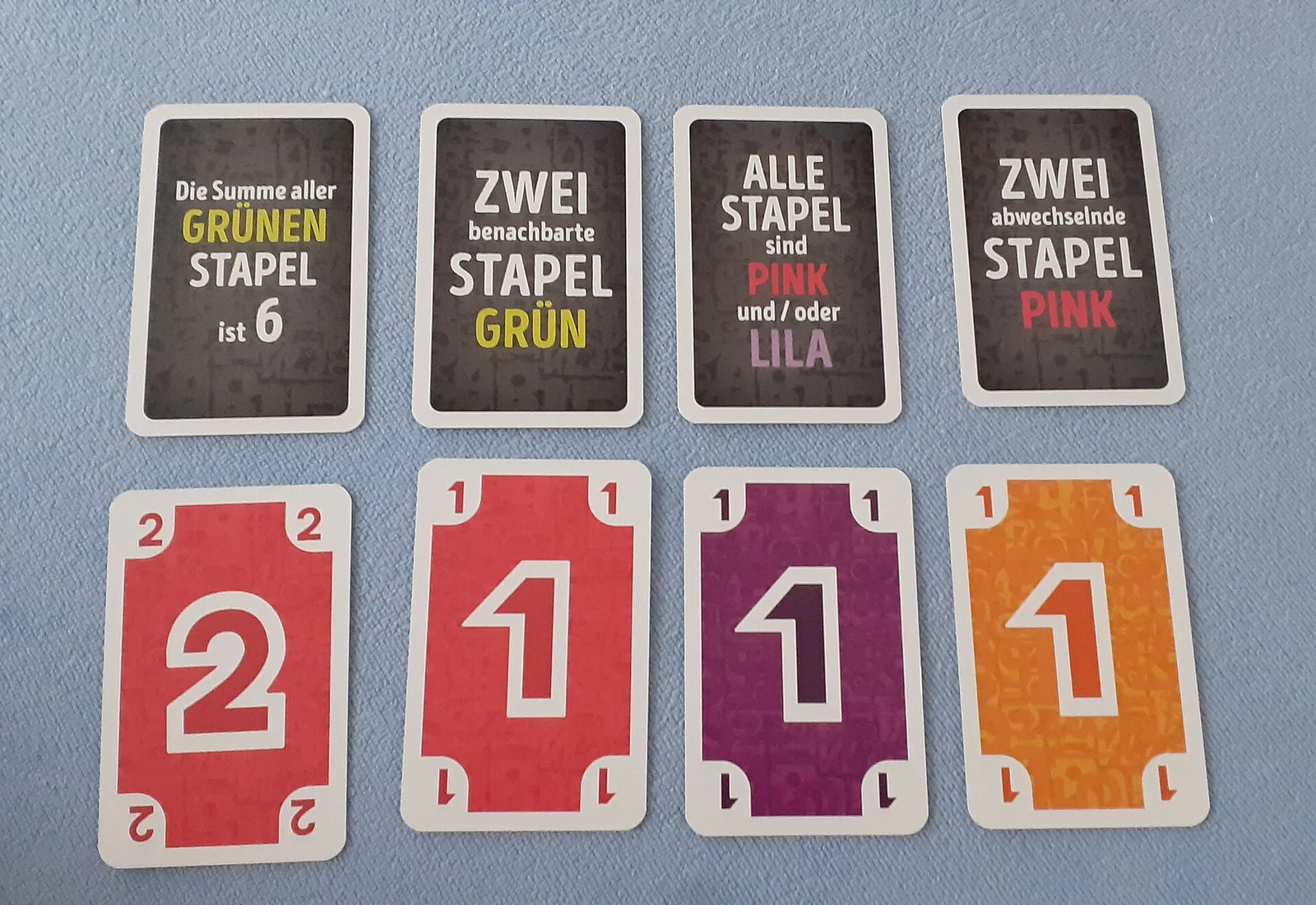 Vier Aufgabenkarten mit deutschen Bedingungstexten über vier bunten Zahlenkarten auf hellblauem Untergrund.