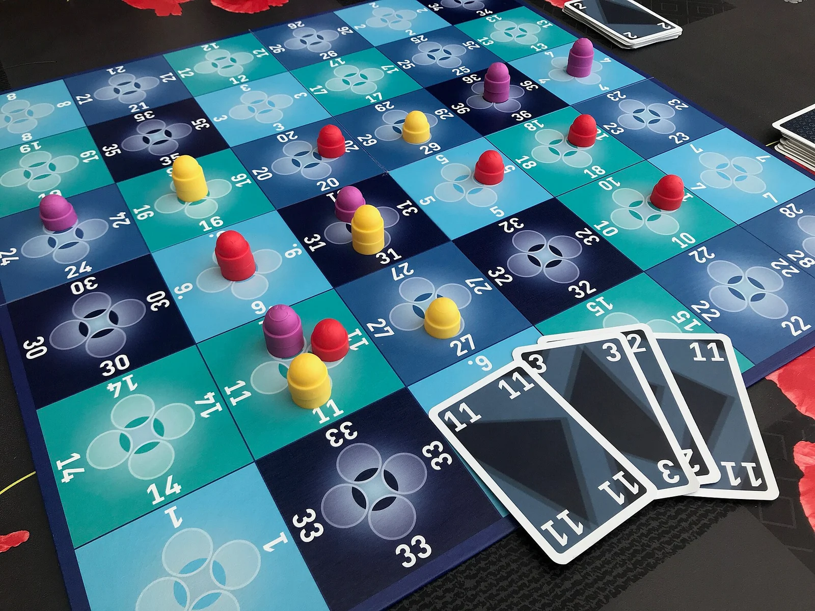 Spielplan mit Feldern von 1 bis 36, verteilten farbigen Setzsteinen und einer Hand aus vier Zahlenkarten.