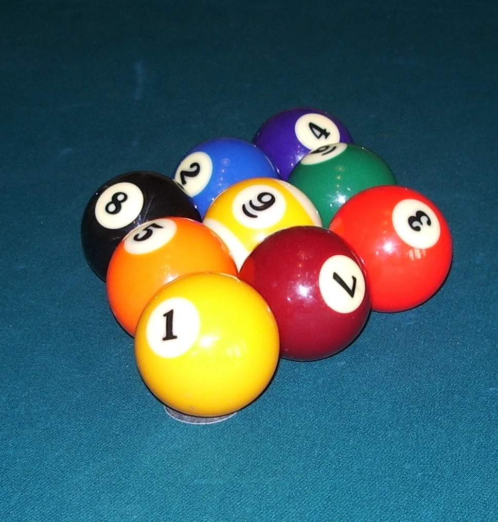 Neun Poolbillardkugeln mit den Nummern 1 bis 9 in Rautenform auf blauem Billardtuch aufgebaut.
