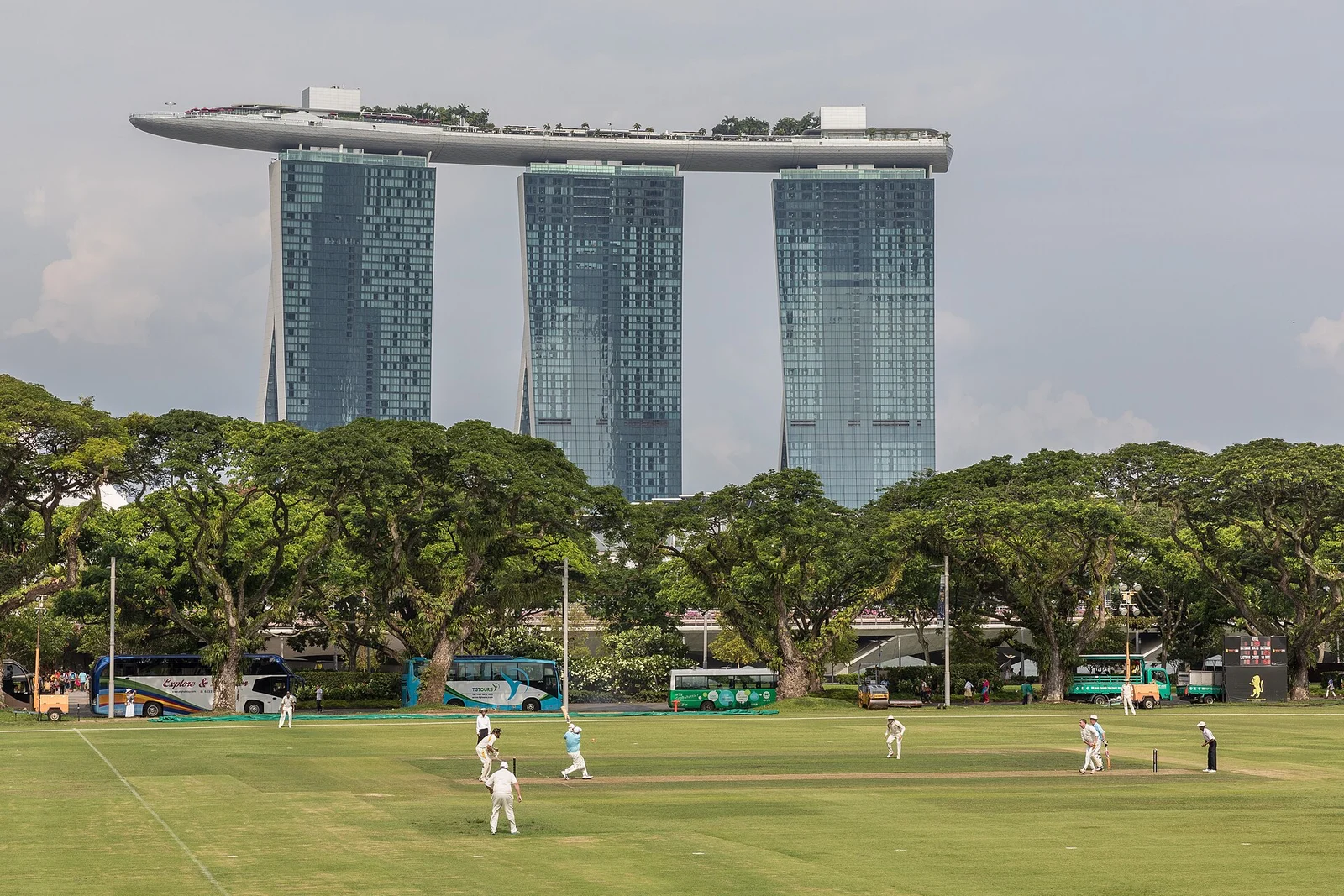 Cricketspiel auf einem großen Rasenfeld vor Hochhäusern in Singapur.