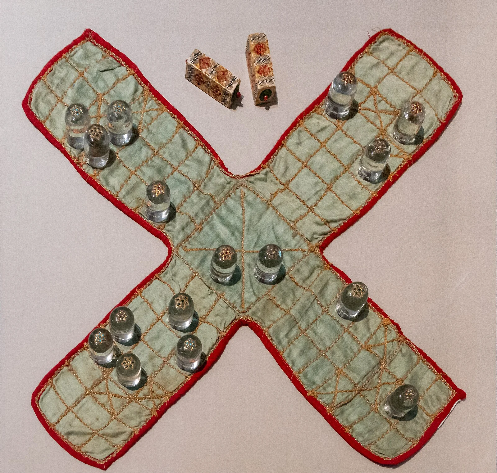 Historisches Pachisi-Set: kreuzförmiges Stofftuch mit Spielsteinen und zwei länglichen Würfeln.