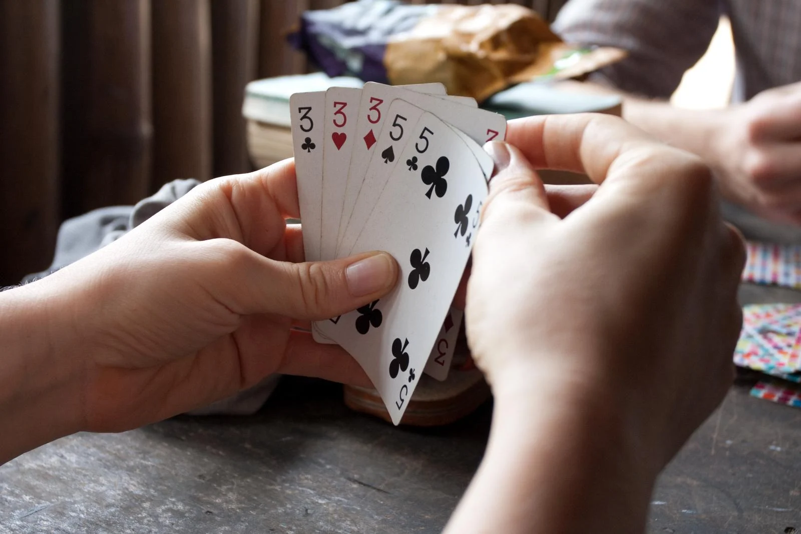 Hände halten aufgefächerte Spielkarten über einem Holztisch.