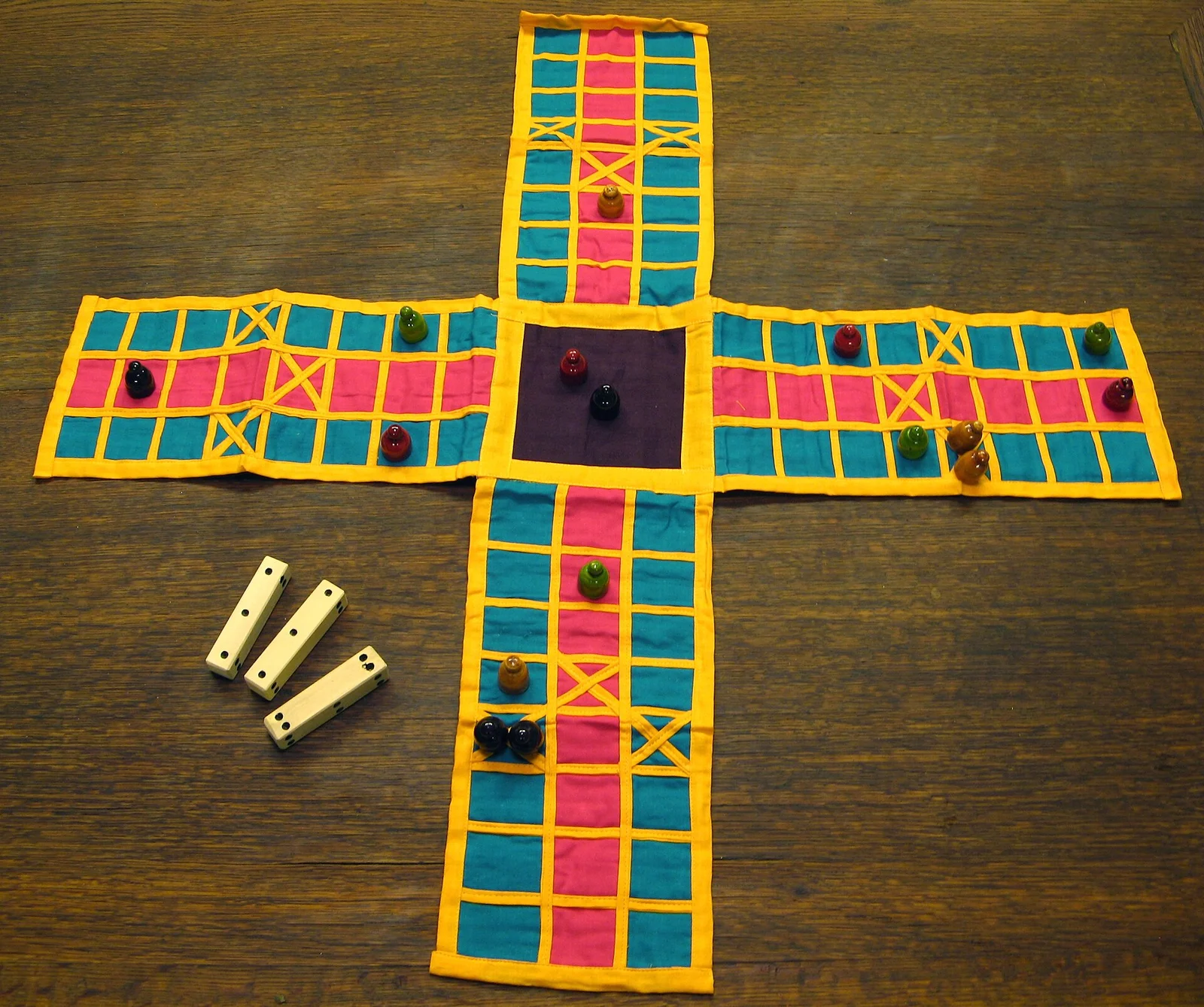 Handgemachtes Pachisi-Replikat aus Stoff in Kreuzform mit Spielkegeln und Stabwürfeln.