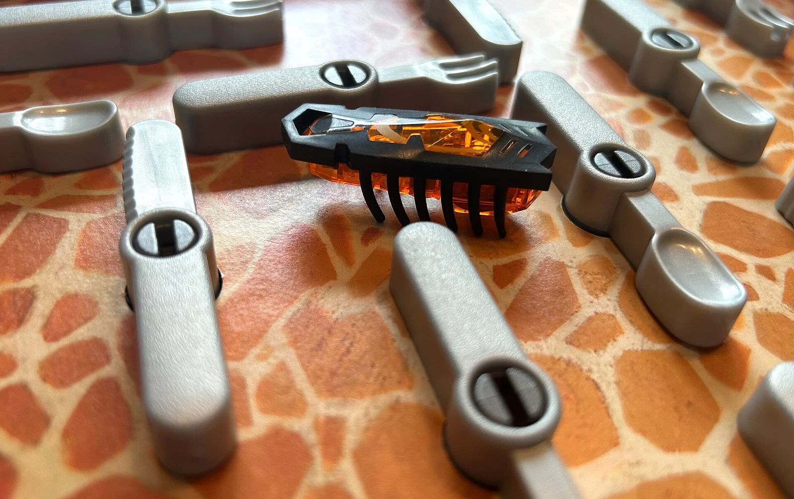 Nahaufnahme der batteriebetriebenen Spielkakerlake zwischen Besteckteilen des Spielplans.