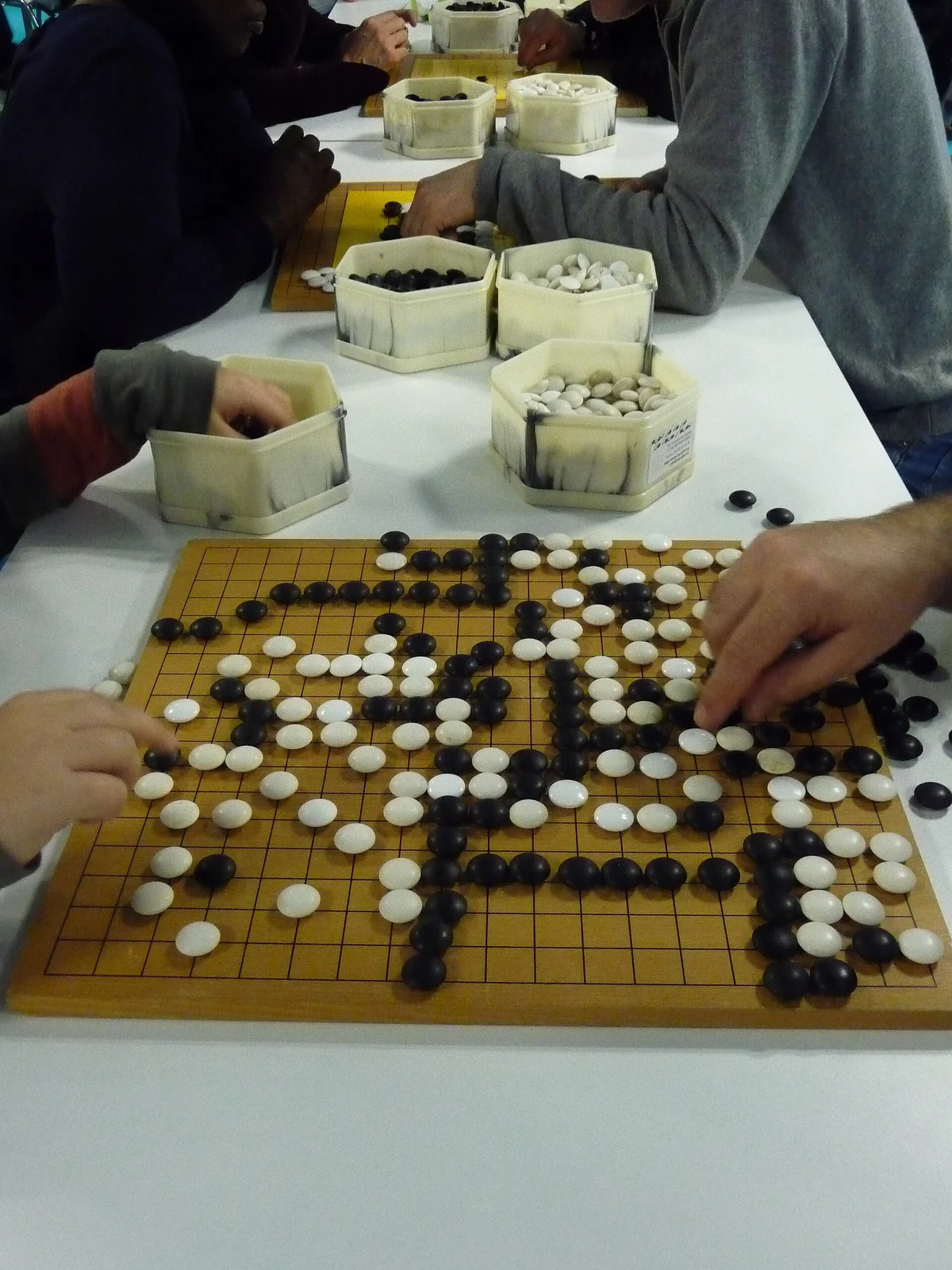 Spieler setzen Steine auf ein Go-Brett bei einem Turnier, daneben Steinschalen.