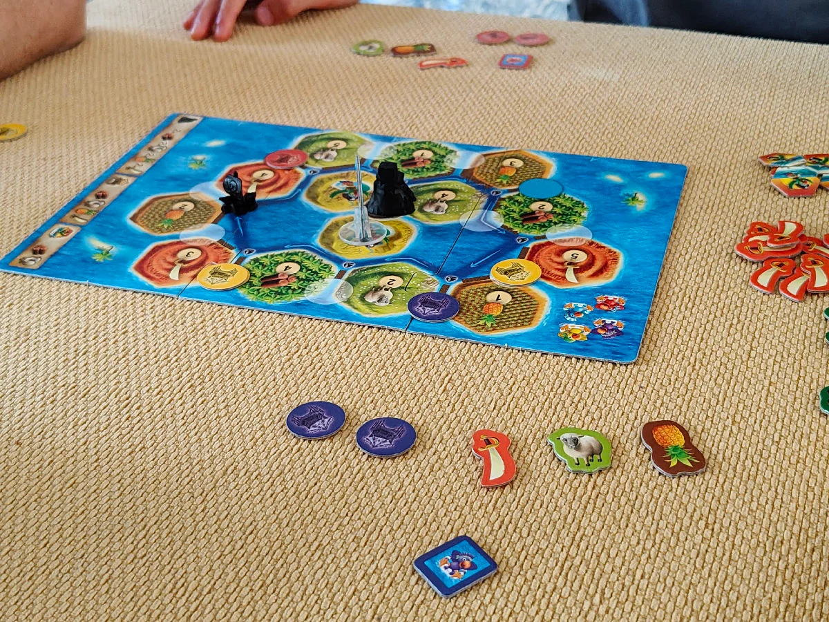 Aufgebauter Spielplan der Reiseausgabe von Catan Junior mit Inseln, Piratenfigur und Rohstoffplättchen auf einem Tisch.