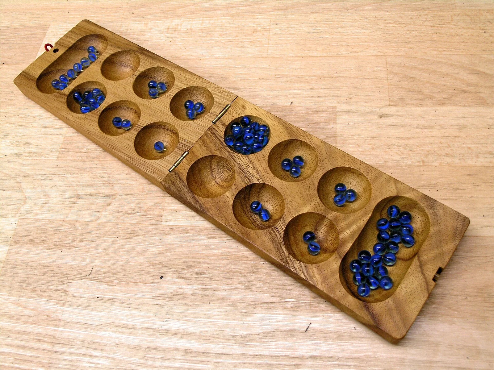 Klappbares Holzbrett mit zwei Reihen zu je sechs Mulden, zwei großen Endmulden und blauen Glassteinen.