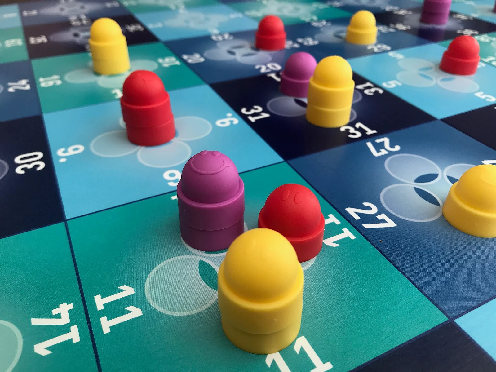 Nahaufnahme eines nummerierten Spielplans in Blau- und Türkistönen mit roten, gelben und violetten Setzsteinen.