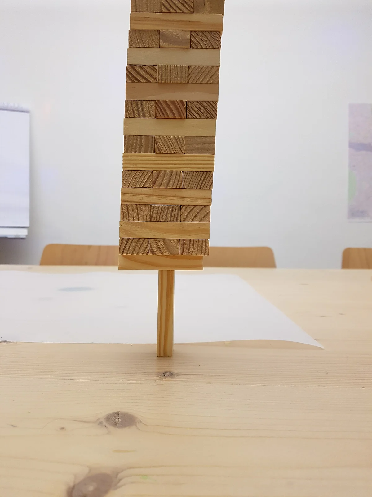 Hoher Turm aus Holzklötzchen, der auf einem einzelnen Stäbchen balanciert, auf einem hellen Holztisch.