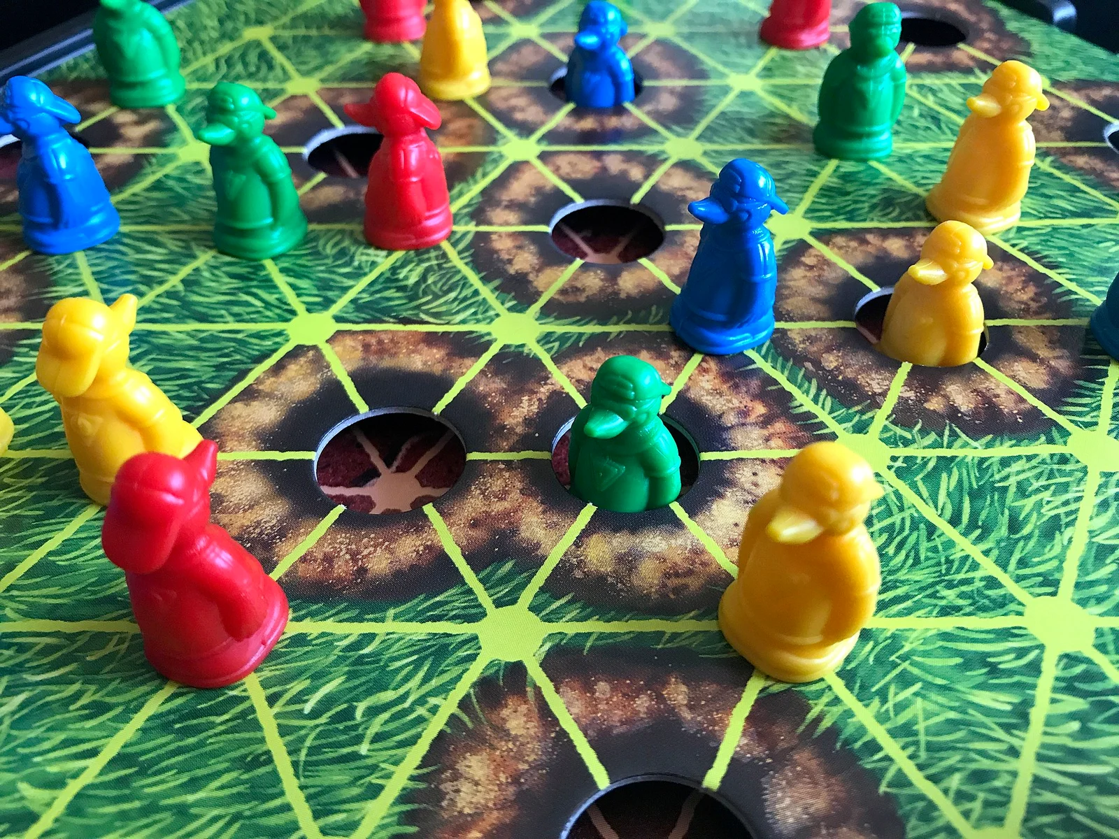 Nahaufnahme eines Spielplans mit Wiesenmotiv, Löchern und bunten Maulwurf-Spielfiguren in Rot, Blau, Grün und Gelb.