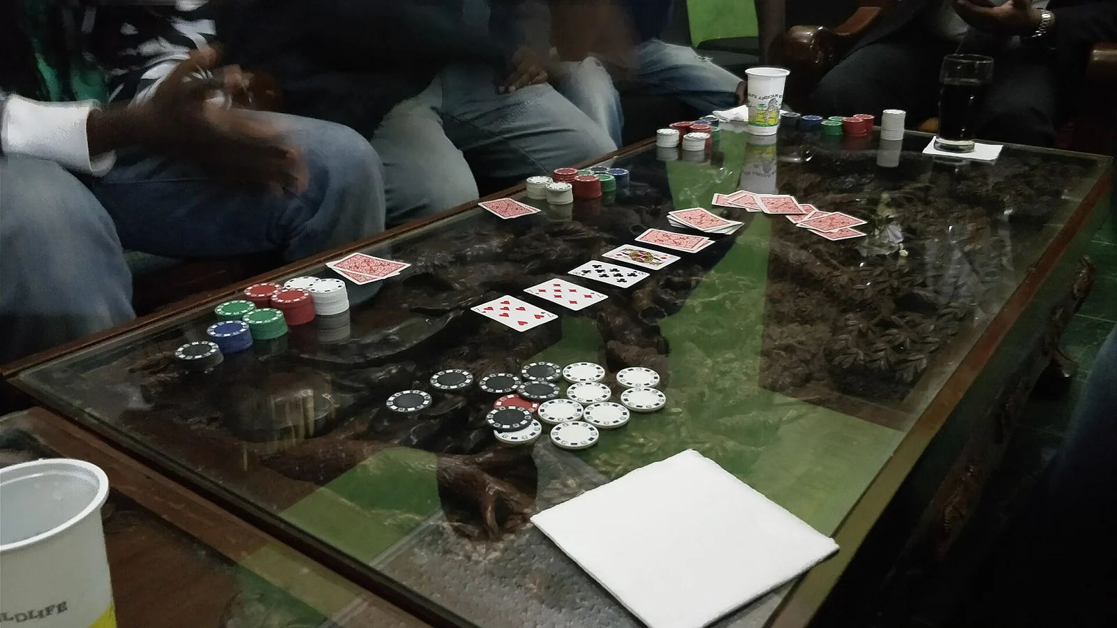 Pokertisch mit offenen Gemeinschaftskarten, Chips und Spielern, deren Gesichter nicht zu sehen sind.
